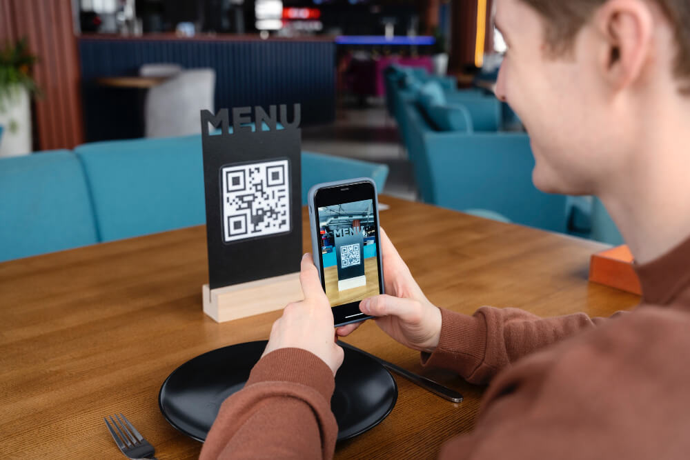 Muž v reštaurácii skenuje QR kód z menu cez svoj smartfón, aby si mohol objednať jedlo digitálne.