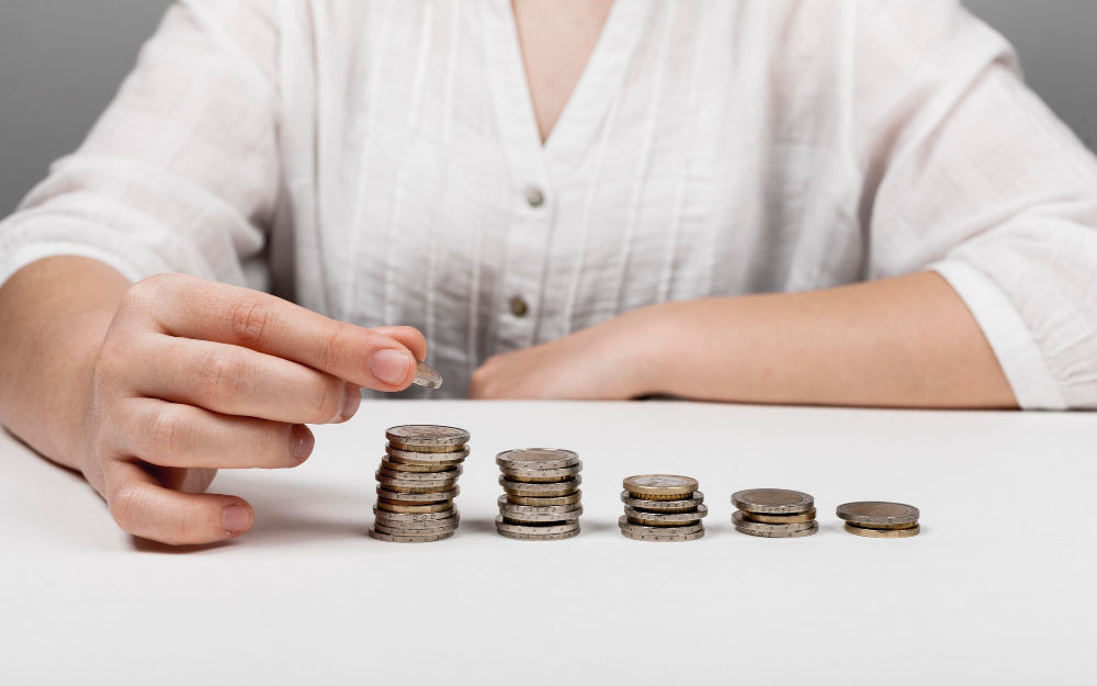 A hand stacking coins into growing piles, symbolizing the effort to reduce costs and improve financial efficiency.